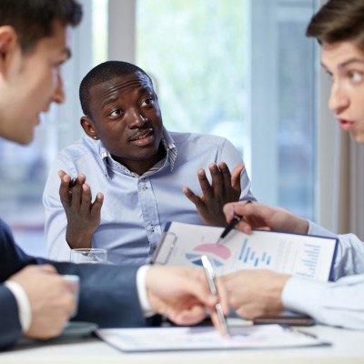 Trois professionnels discutant intensément au bureau pour résoudre un conflit, avec des graphiques et documents devant eux